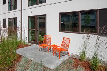 Two orange chairs are placed on a concrete slab outside a building.